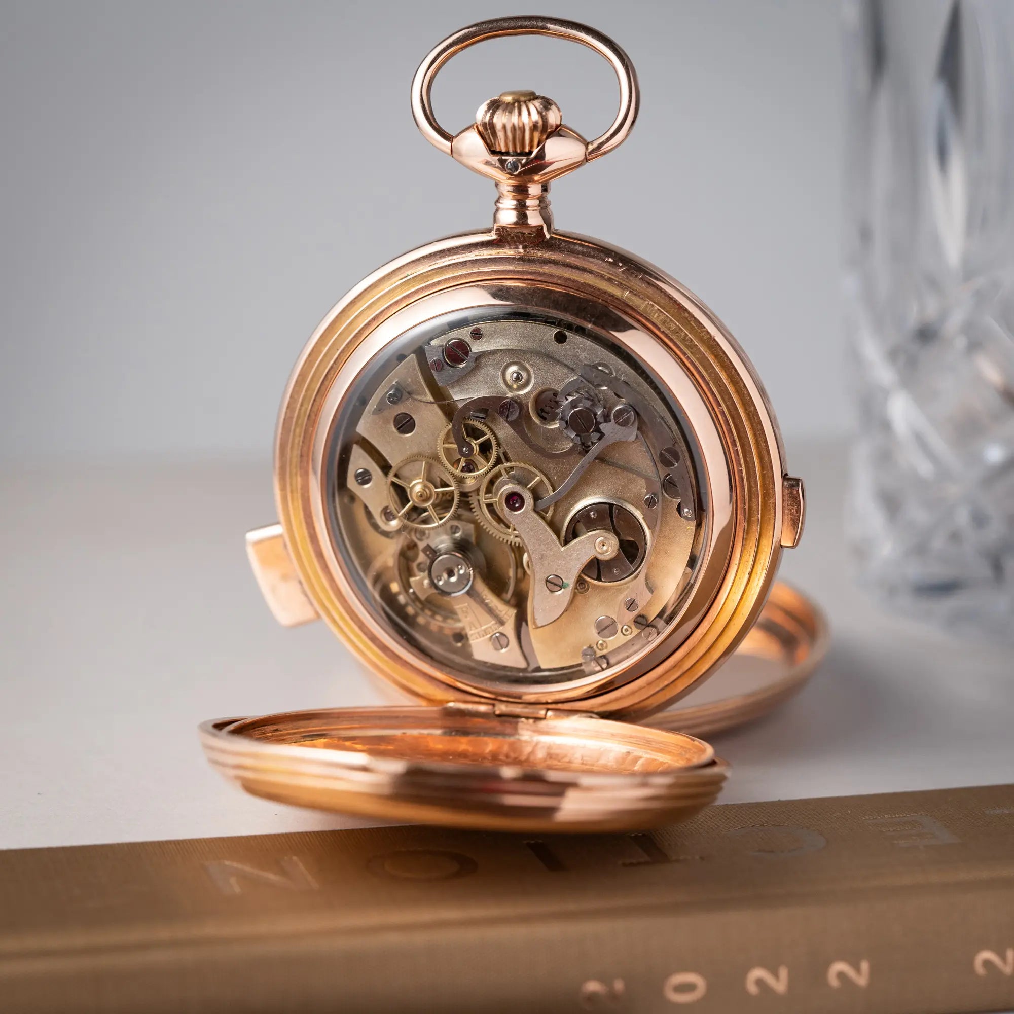 Produktfotografie zeigt die Vollkalender Taschenuhr aus 14 Karat Roségold mit viertel Stunden Repetition und Mondphase-Anzeige bei 6 Uhr mit geöffnetem Gehäusedeckel, wodurch das Handaufzugs-Caliber sichtbar ist