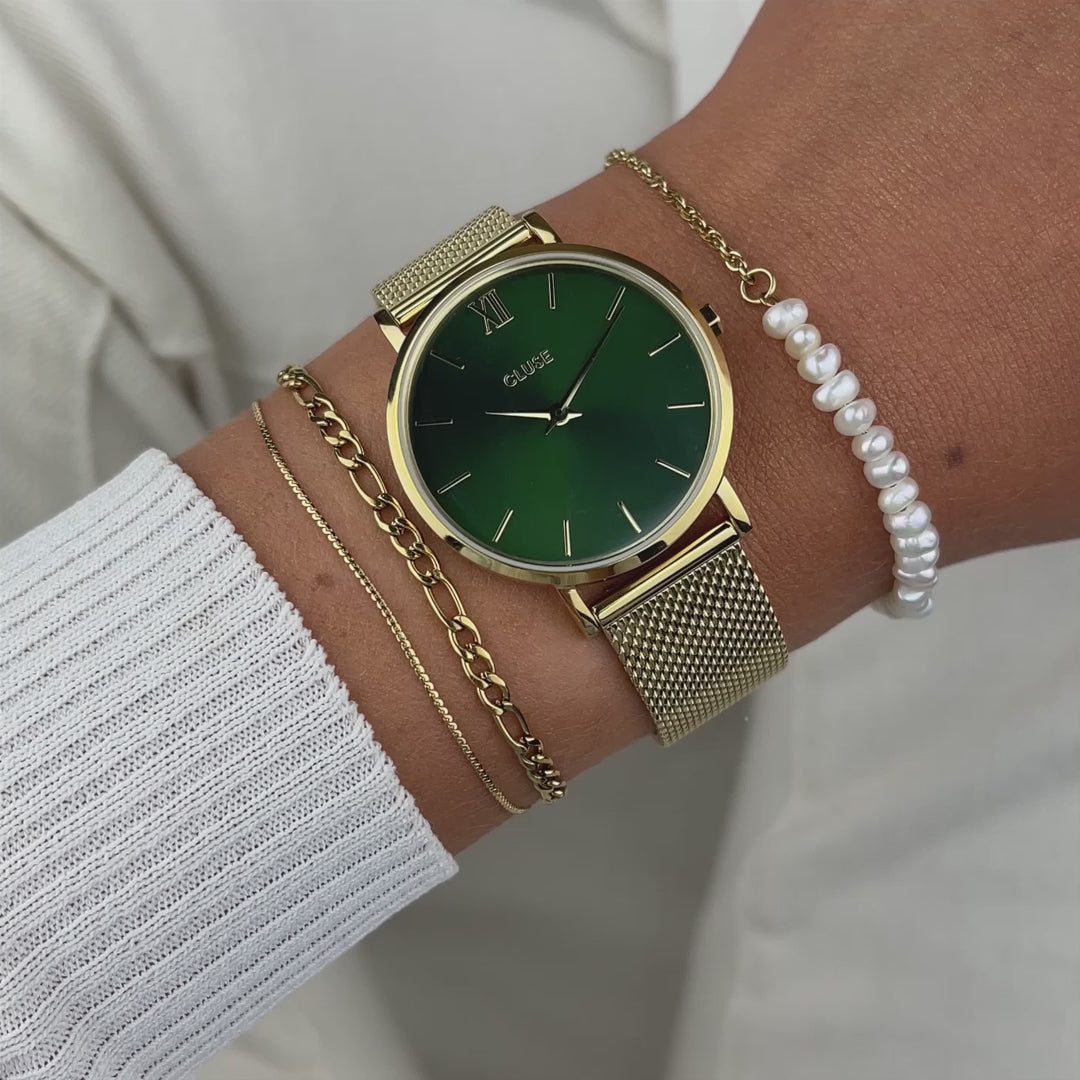 Wrist-Roll der Cluse Stahl-Uhr "minuit Mesh" mit gelbgolden-farbigen Gehäuse mit grünem Zifferblatt an einem Frauen-Handgelenk