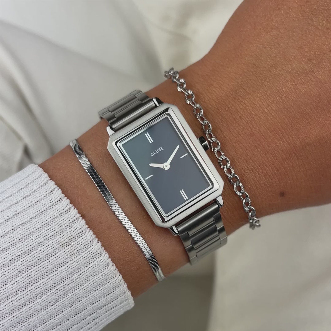 Frau präsentiert die Cluse "Fluette" Stahl-Uhr mit dunkelblauem Zifferblatt mit silberfarbenem Gehäuse per Wrist-Roll